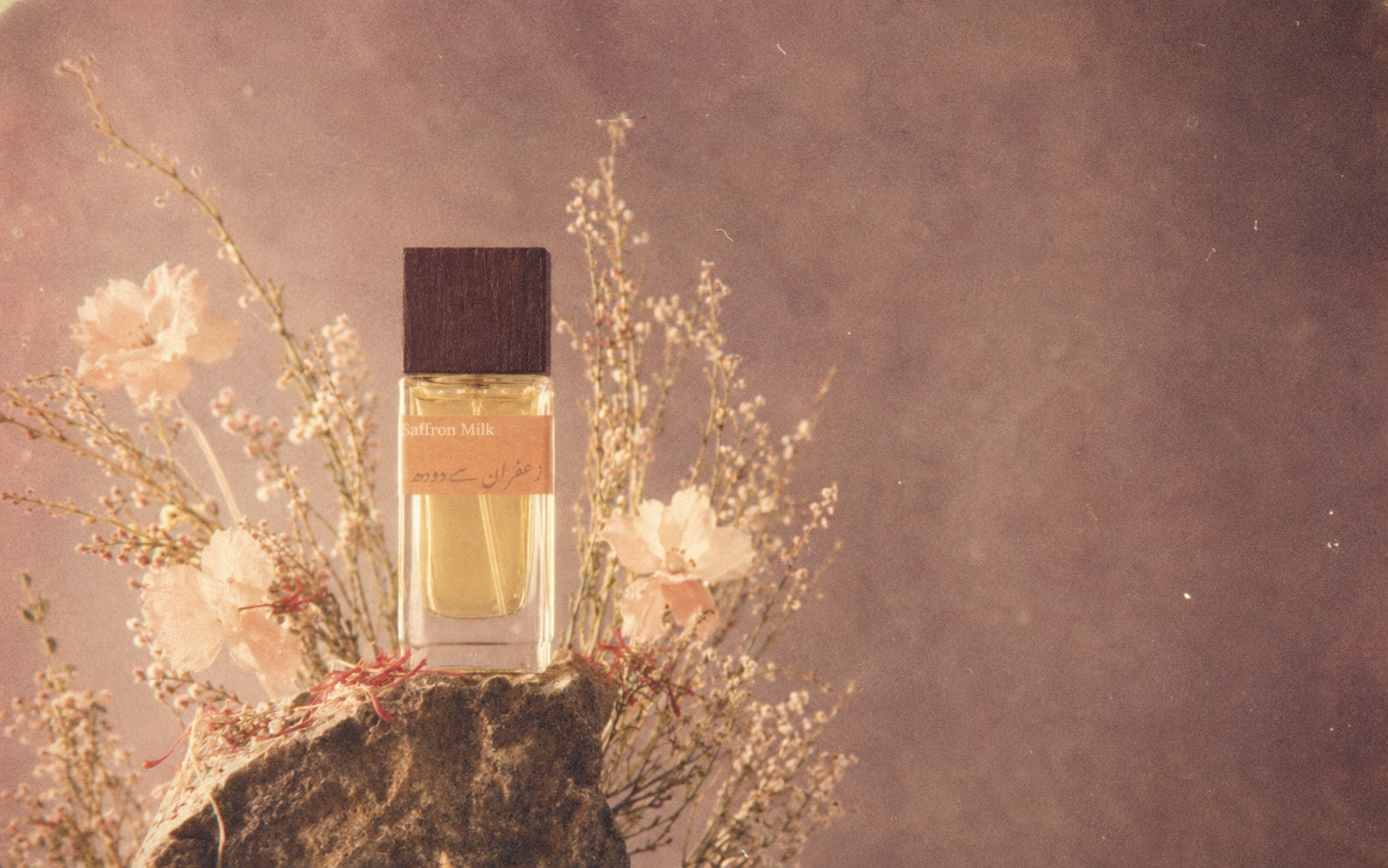 Azahrah Saffron Milk perfume on stone among flowers in warm light.