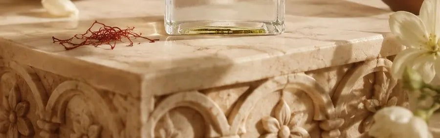 Detail of an Azahrah photograph: carved stone, a row of small flowers cut inside shallow arches, with saffron threads and the foot of a perfume bottle resting on the ledge above.