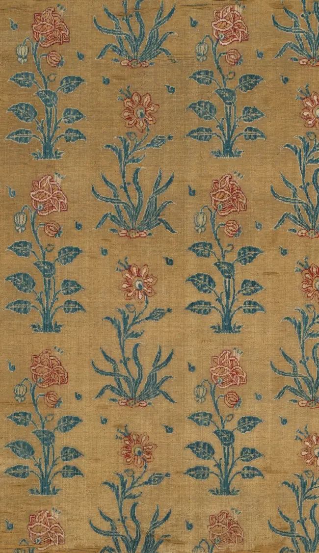 A detail of a Mughal velvet panel: rows of the same flowering plant, red blooms on blue-green stems, repeating across a worn gold ground.